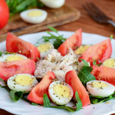Tavuk ve yumurta ile kolay sebze salatası. Domates dilimleri, roka, bıldırcın haşlanmış yumurta, tavuk göğsü ve beyaz bir tabak ve ahşap arka plan baharat salatası. Rustik tarzı. Portre