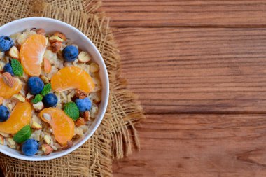 Sağlıklı Topingler ile yulaf lapası. Mandalina, yaban mersini, fındık ve nane beyaz bir kase ve kopya alanı ahşap bir zemin üzerine yulaf ezmesi. Kilo kaybı için basit yulaf lapası tarifi. Üstten Görünüm