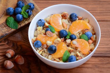 Lezzetli ve sağlıklı yulaf lapası meyve, çilek ve fındık ile. Taze mandalina, yaban mersini, fındık ve beyaz bir kase içinde nane ev yulaf ezmesi. Yulaf lapası yulaf tarifi. Rustik tarzı. Portre