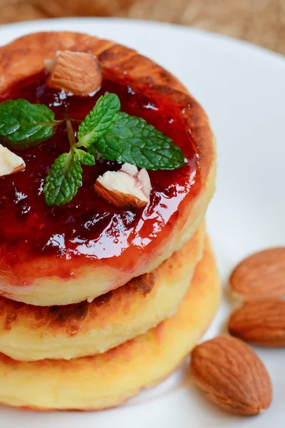 Quarkkuchen. gebratene Quarkkuchen mit Marmelade und Mandeln auf einem weißen Teller. traditionelles ukrainisches Dessert syrniki Rezept. vertikales Foto. Nahaufnahme — Stockfoto