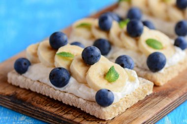 Ev yapımı crispbread tost süzme peynir, muz ve çilek ahşap tahta üzerinde. Süzme peynir sandviç fikir. Portre