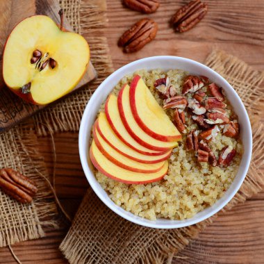 Quinoa kahvaltı kase meyve ve fındık ile. Gluten free quinoa yulaf lapası taze elma ve pecans beyaz bir kase ve ahşap arka plan ile. Rustik tarzı. Portre. Üstten Görünüm