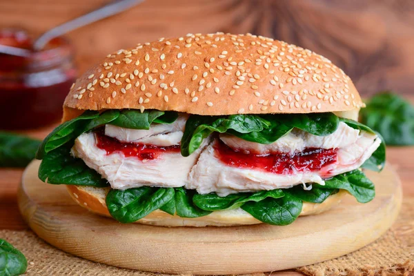 Crispy chicken fillet burger recipe. Simple chicken burger with fresh spinach and berry jam on a wooden board. Closeup