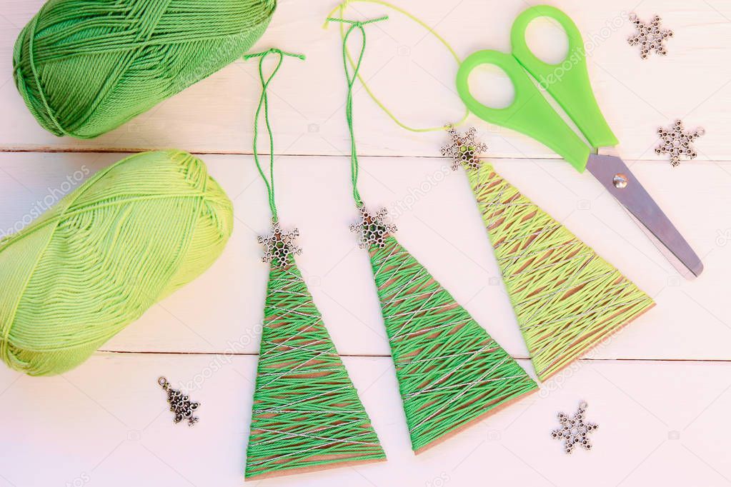Christmas trees ornaments on a wooden background. Simple Christmas trees ornaments made of old cardboard box and cotton yarn. Creative recycling idea for home or school. Easy recycled crafts. Recycling projects for school. DIY Christmas tree ornament