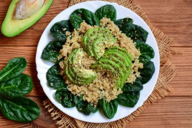 Baharatlı quinoa yulaf lapası. Vegan quinoa ile beyaz bir tabak ıspanak ve Avokado salatası. Kahverengi ahşap masa. Rustik tarzı. Üstten Görünüm. Quinoa avokado kahvaltı kase. Avokado quinoa tarifi. Hasat kase tarifi. Sebze kase tarifi