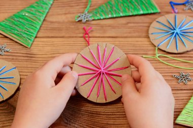 Child is holding a Christmas ball ornament in his hands. Child is showing a Christmas ball ornament. Easy recycled crafts and activities for kids. DIY Christmas ornaments. Recycled Christmas decoration. Christmas ornaments card. Holiday background.