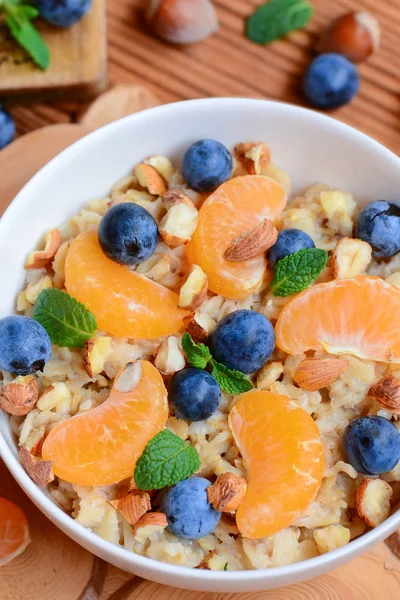 Taze mandalina, meyveler, fındık ve nane beyaz bir kase ve ahşap arka plan üzerinde basit yulaf lapası. Quinoa yulaf lapası vegan. Hızlı quinoa yulaf lapası. Quinoa yulaf lapası yavaş tencere. Quinoa yulaf lapası mikrodalga