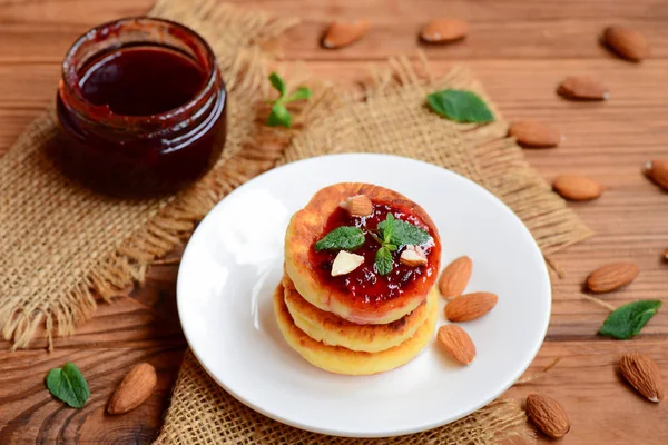 Fried cottage cheese fritters with berry jam, almonds nuts and mint on a served plate. Yummy cottage cheese almond flour fritters. Healthy cottage cheese. Homemade cheese fritters. Fried cheese fritters. Sweet syrniki dessert. Fried cheese cakes