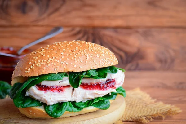 Healthy burger with boiled chicken, berry jam and fresh spinach. Easy and wholesome chicken burger on a wooden board. Rustic style. Homemade chicken breast burger. Chicken burger photo. Homemade chicken burger idea