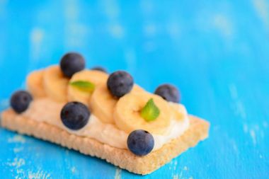 Crispbreads tatlı süzme peynir, taze muz, çilek ve mavi ahşap zemin üzerine nane. Portre