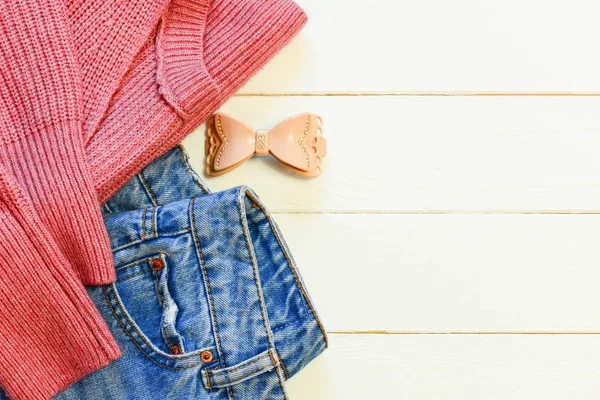 Womens casual clothes. Female blue jeans, knit pink sweater, hair grip on a wooden background with empty space for text. Top view. Cute casual outfit. Casual outfit for work. Casual outfit idea with jeans. Casual wear for ladies