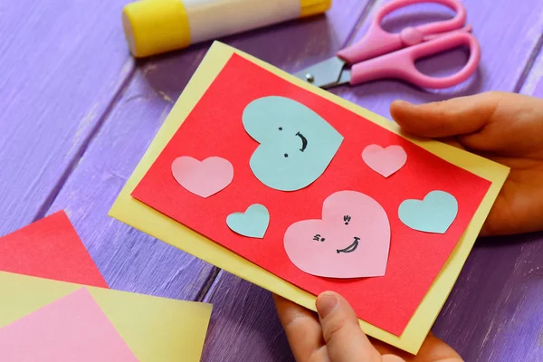 Child is holding a Valentines card in his hands. Child is showing a greeting card. Happy Valentines Day card. Easy paper crafts for kids concept. Closeup. Valentines Day card. Valentines Day greeting card. Birthday cards handmade diy paper crafts