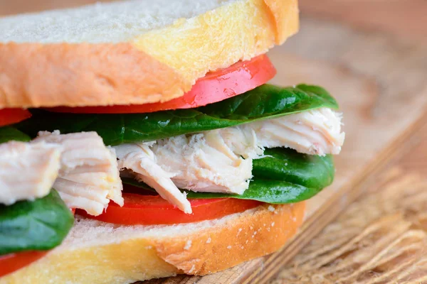 Healthy sandwich idea. Chicken sandwich with fresh tomatoes and spinach leaves on a brown wooden board. Rustic style. Closeup. Simple chicken sandwich. Healthy chicken sandwich recipe