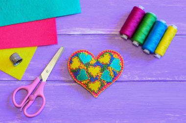Embroidered heart for Valentines Day. DIY stuffed embroidered Valentines Day felt heart, thread set, scissors, thimble, colorful felt sheets on a purple wooden background. Hand sewing hobby. Top view. Easy sewing hobby. Sewing projects for beginners