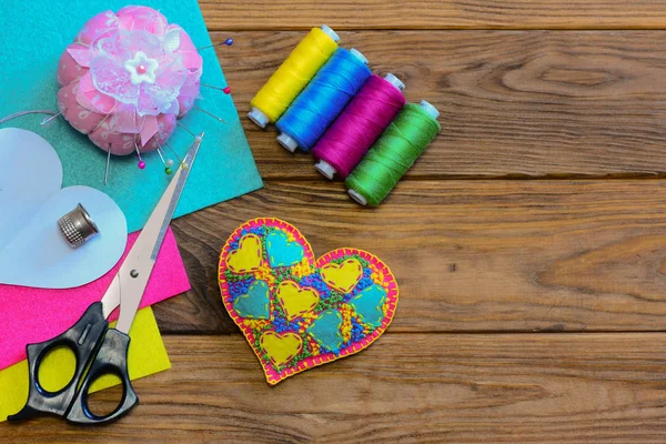 Valentines Day heart. Colorful felt heart, thread set, scissors, thimble, colorful felt sheets, paper template on a wooden background with copy space. Top view. Valentines day homemade crafts. Valentine day crafts for preschoolers