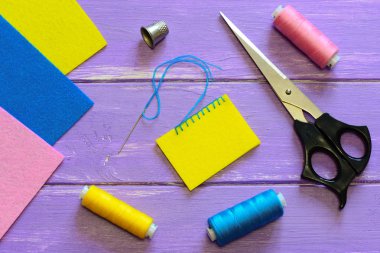 Closed blanket stitch by hand. Easy blanket stitch pattern. Colourful felt sheets, thread set, thimble, scissors on a wooden background. To join pieces of felt. Top view. Joining felt pieces. Closed blanket stitch edging. Sewing education for kids