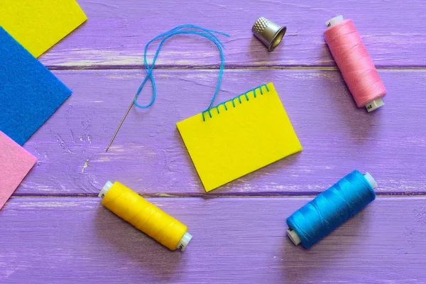 Closed blanket stitch edging. Easy blanket stitch variation. Colourful felt sheets, thread set, thimble on a wooden background. Hand sewing felt. How to sew felt pieces. Top view. Joining felt pieces. Closed blanket stitch edging