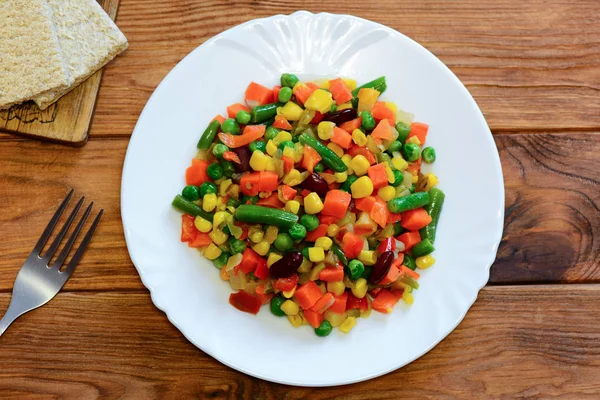 Mixed vegetable stew on a serving plate and wooden table. Homemade stewed carrots, green beans, red beans, peas, corn, pepper and onions. Healthy vegetarian stew. Top view. Winter vegetable stew. Fall vegetable stew