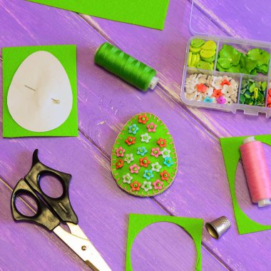 Plastik çiçek ve boncuk ile parlak Paskalya yumurta dekorasyon. Yumurta el sanatları, makas, iplik, kağıt şablonu, yüksük mor ahşap masa üzerinde hissetti. Paskalya DIY dekor için fikir. El dikiş projeler. Yeni başlayanlar için dikiş fikir. Okul öncesi için dikiş