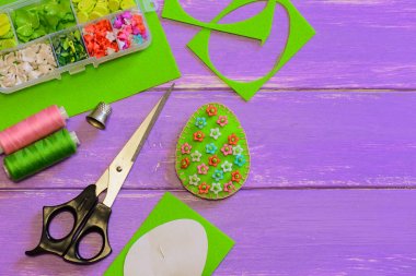 Paskalya yortusu yumurta dekor plastik çiçek ve boncuk ile hissettim. Yumurta el sanatları, makas, iplik, kağıt şablonu metin kopyalama yeri olan mor ahşap arka plan üzerinde hissetti. El dikiş projeler. Yeni başlayanlar için dikiş fikir. Okul öncesi için dikiş