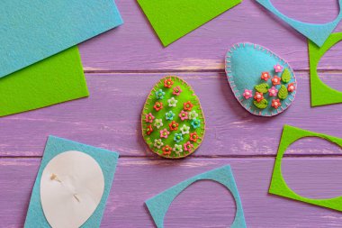 Sanat Paskalya yumurtası süslemeleri plastik çiçekler ve yapraklarla süslenir. Yumurtalar solmuş, çiçek desenleri, keçeli çarşaflar, ahşap masadaki kağıt şablonlar. Çocukların Paskalya dekorasyonu fikri. Kolay dikiş. Terzi, konsept dikiş işyeri. El dikimi konsepti çalışma yeri