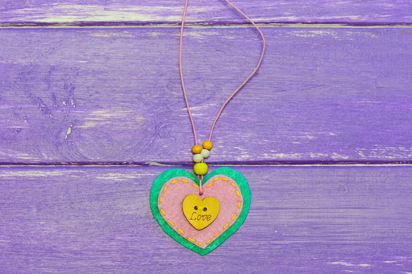 Heart shaped jewelry for Valentine\'s Day. Valentines day felt heart jewelry isolated on the purple wooden background. Cute gift for Mothers day or moms birthday. Valentines day gifts for mom homemade. Valentine\'s day gifts for mom diy