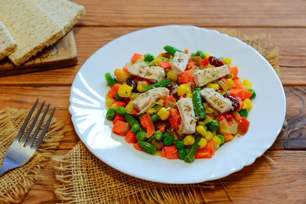 Chicken breast and mixed vegetable stew on the serving plate and the wooden table. Low-calorie chicken vegetable stew. Stewed carrots, green beans, peas, corn and pepper with boiled chicken breast. Chicken breast and vegetable stew