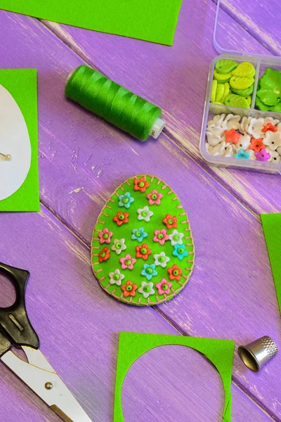 Pretty green Easter egg decoration with bright floral pattern. Felt egg decoration, scissors, paper template, thread, plastic box. Handmade workshop for kids. How to hand sew a simple felt Easter egg. Making felt Easter egg. Sewing felt Easter egg