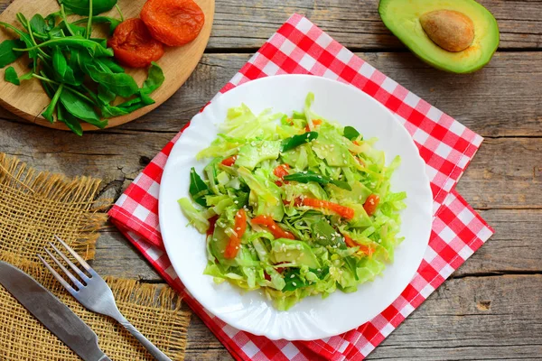 Healthy cabbage avocado salad. Easy fresh cabbage salad with avocado, dried apricots, ruccola and sesame on a plate and on wooden background. Summer vegan diet salad. Raw salad dressing recipe. Raw salad recipes indian. Raw vegetable salad