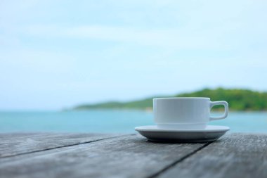 Mavi deniz ve mavi gökyüzü görünümü arka planda yaz ile ahşap masa üzerinde kahve fincanı.