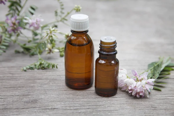 Coronilla varia essential (tincture, remedy, infusion) oil glass bottle on wooden background with fresh Coronilla varia flowers — Stock Photo, Image