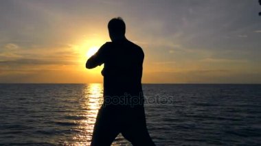 Adam kendini savunma tekniği denizde günbatımında pratiği yapıyor. Kendini savunma eğitim yalnız.