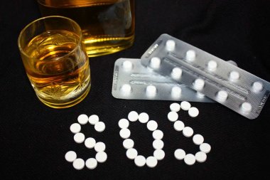 White pills on black background, which forming the word SOS, with glass and bottle of alcohol. Benzodiazepines suicide combination or addiction narcotic concept. clipart