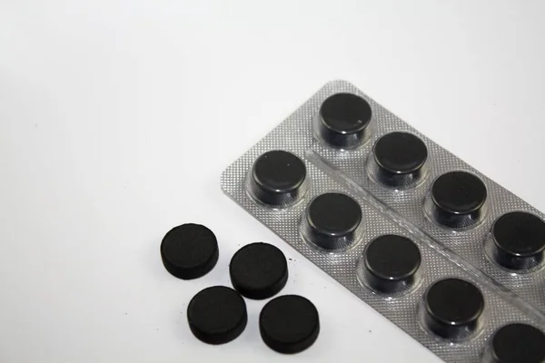 Activated charcoal ronde zwarte tabletten pillen en blister op witte achtergrond — Stockfoto