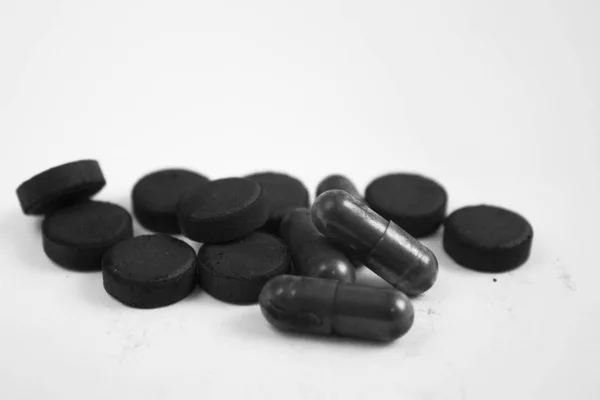 Kohle schwarze Kapseltabletten und Pillen in einem Haufen auf weißem Hintergrund — Stockfoto