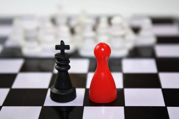 Černý král a červená dáma královna figurky z člověče nezlob se a bílé rozmazané šachové figurky v dálce. Na šachovnici zajímavý koncept. — Stock fotografie