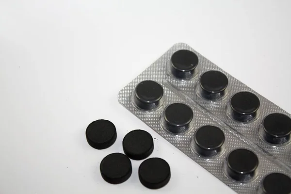 Активоване вугілля навколо чорних таблеток таблетки і блістер на білому тлі Стокова Картинка