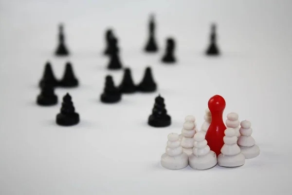 Dvě skupiny šachové figurky a jeden červený ludo figurka střední bílé skupiny. — Stock fotografie
