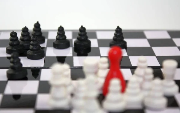 Šachová partie s selektivní fokus na černý pěšec kousky s rozmazané bílé skupiny s červenými ludo postavu vůdce. Soutěž společnosti nebo konflikt národností. — Stock fotografie