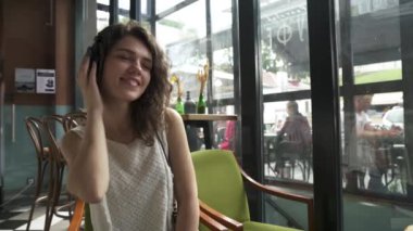  Kıvırcık saçlı kız kulaklıkla müzik dinler ve bir yaz kafesinde dans eder.