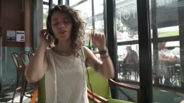  Kıvırcık saçlı kız kulaklıkla müzik dinler ve bir yaz kafesinde dans eder.