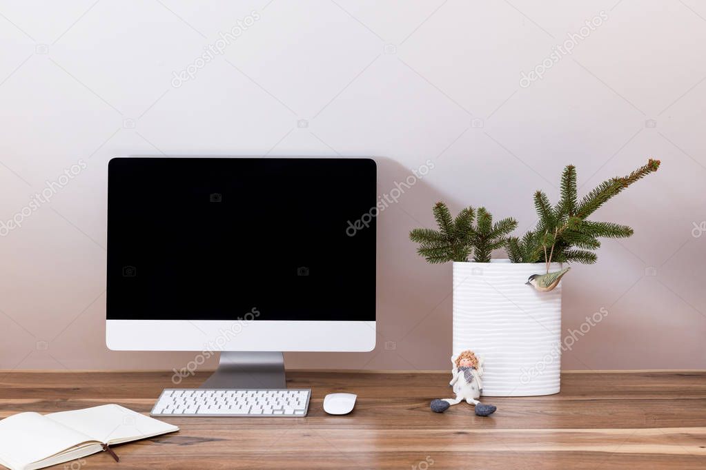 Modern workspace. Computer and a notebook on a wooden walnut table. A vase with a fir branch for christmas mood.