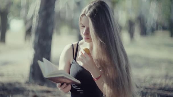 4k junge Frau liest Buch und isst Obst im Park — Stockvideo