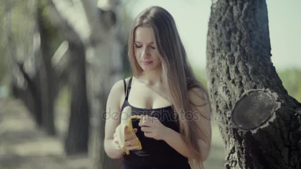 4K молодая девушка ест банан в парке — стоковое видео
