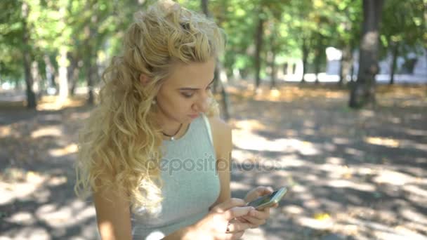 女の子に座ってベンチの公園 スマート フォン メッセージのテキスト メッセージ — ストック動画