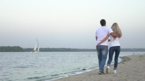 スローモーションのカップルが手を繋いでいるを楽しむビーチの上を歩くと — ストック動画
