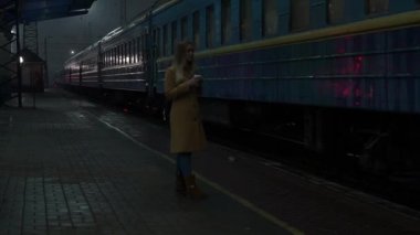 Gerçek zamanlı sarışın genç kadın beklediği Tren İstasyonu saatler numaralı treni