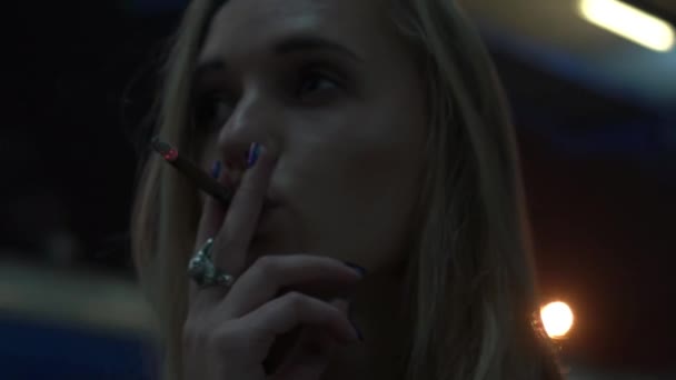 Une jeune femme réfléchie fume une cigarette dans la ville la nuit Gros plan 