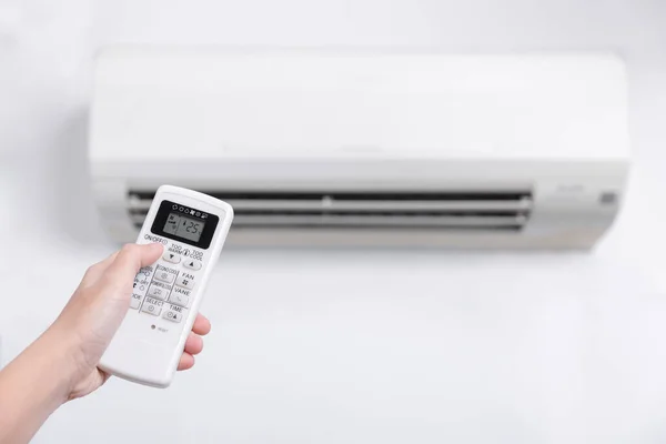 Close-up of men hand operating air conditioner with remote control, Close up shot of hand holding the remote control of  white air conditioner on white color wall.