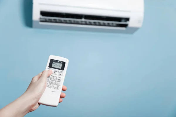 Close-up of men hand operating air conditioner with remote control, Close up shot of hand holding the remote control of white air conditioner on blue color wall.